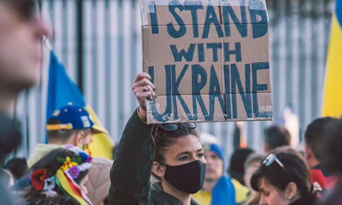 A person holding up a 'I Stand With Ukraine' sign - Unsplash